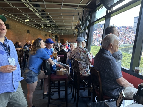 a large group of people sitting in tall chairs watch a baseball game through a window