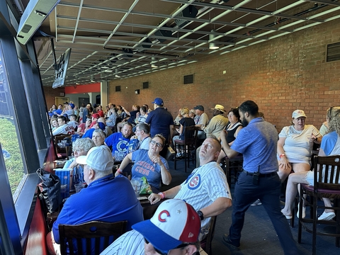 a large group of people enjoy an indoor suite while watching a baseball game