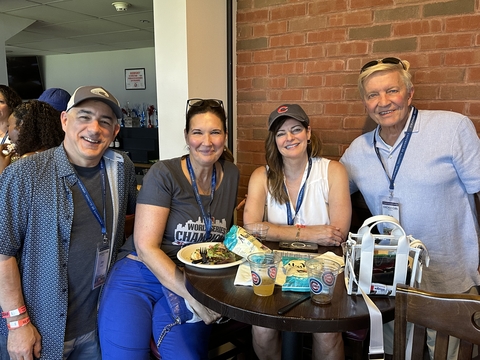 four people pose for a picture at a high top table while enjoying some food