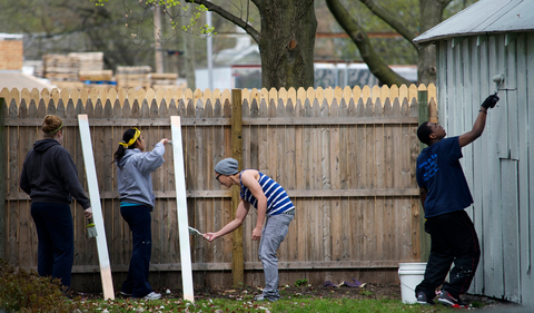 four people work to paint a fence and a building