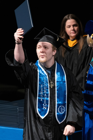 male graduate holding up degree on stage
