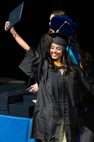 female graduate holding up degree on stage
