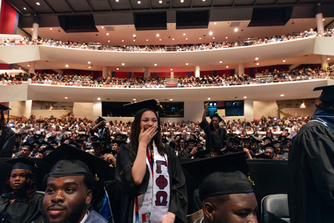 graduate with hand over mouth watching commencement