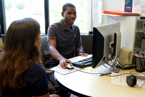 an advisor at his computer with a student sitting next to him