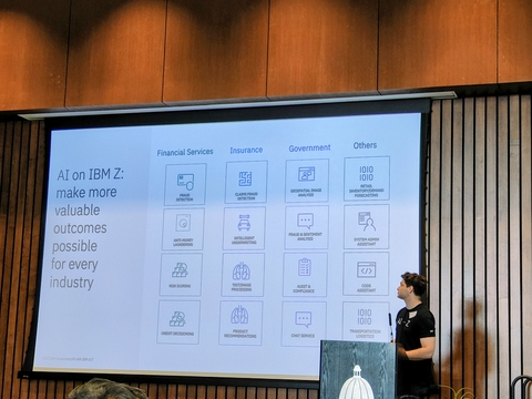 Lucas Sahn from IBM Z, stands next to a large screen displaying a grid of AI use cases for various industries, including financial services, insurance, and government.