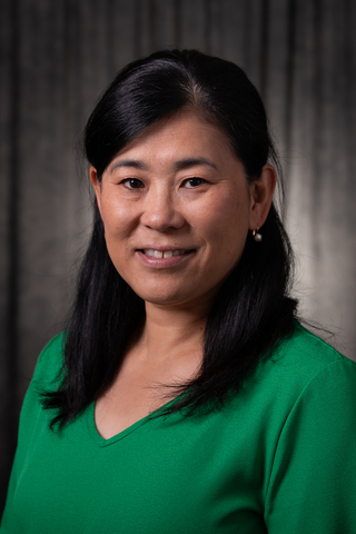 Woman in a green shirt smiling against a dark background.
