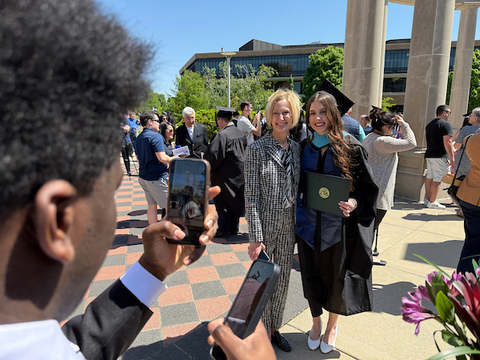 Chancellor poses with a student in commencement regalia in front of the colonnade
