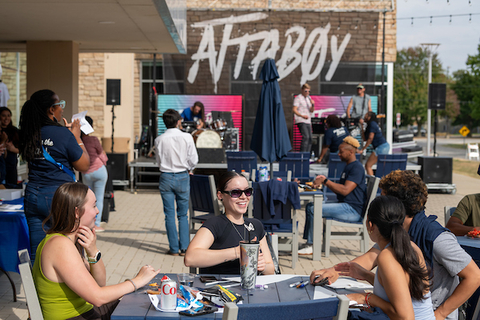 Student talk joyfully at an outdoor event with live music.