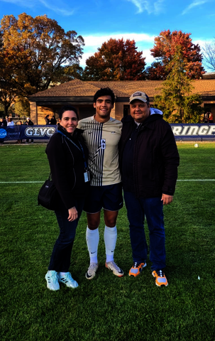 Lucas standing with his parents in his soccer uniform on the soccer field.