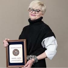 Woman with short hair holding a framed certificate, smiling.