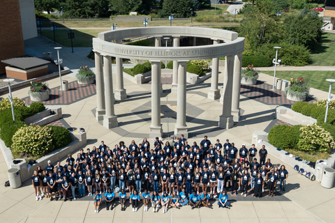Large group of UIS students gathered in front of the University of Illinois Springfield colonnade on campus.