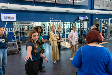 Group of people in a gym, one woman gesturing with her hand.