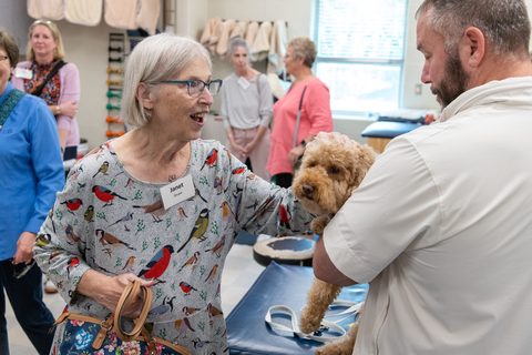 woman smiling while petting a small dog held by a man in a clinic setting.