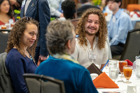 Three people smiling and chatting at a luncheon event.