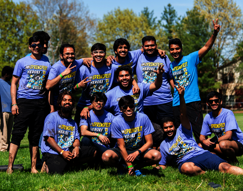 A group of men in purple t-shirts pose for a photo in the sun.