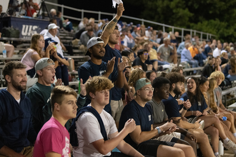 Students standing and clapping during a soccer game. 