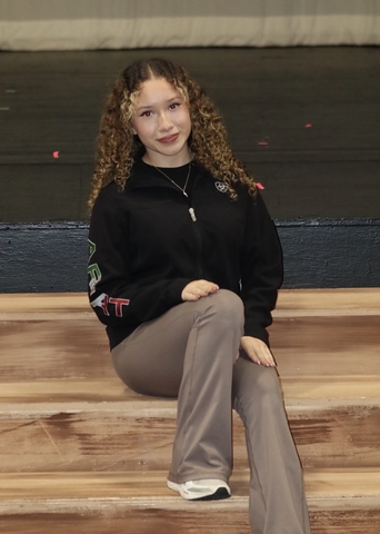 student posed seated on a wooden floor