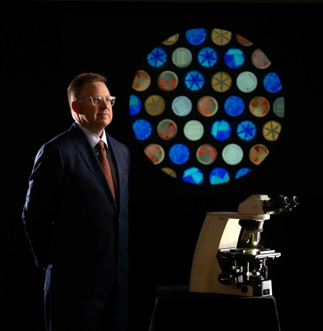 Noah Reynolds in suit and tie with laboratory equipment and microbiology graphic