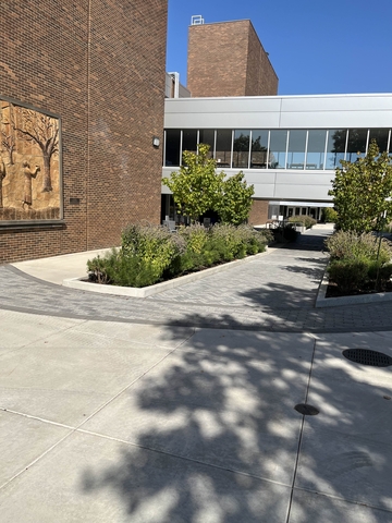 A brick-paved walkway that goes underneath a catwalk.