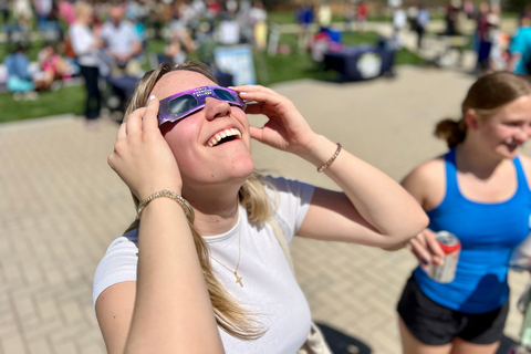A student smiles while looking up at the sky through eclipse glasses during a solar eclipse viewing event.