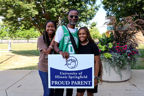 parents holding a UIS proud parent sign with student