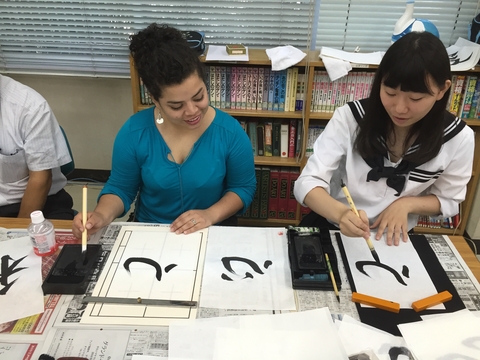 Two young ladies painting calligraphy with black ink on white paper