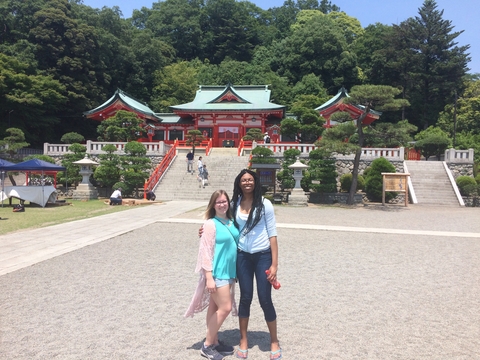 Two female students posing outside a Japanese structure in the sunshine