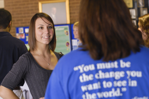 Two people talking to each other, with the back of one shirt with text "You must be the change you want to see in the world"