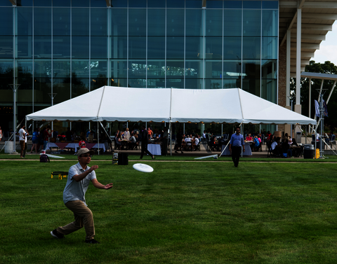 A guy playing Frisbee in front of a white tent in front of the Union. There are groups of students under the tent.