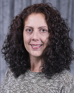 Smiling woman with curly hair against a gray backdrop.