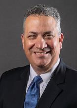 Professional portrait of Athletic Director Mike Hermann wearing a blue tie and dark suit.