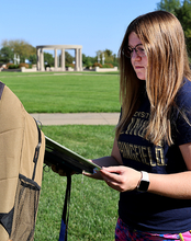 A student reads a story about suicide attached to a backpack on the quad.