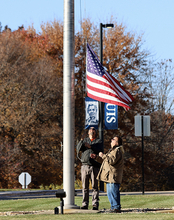 Two veterans raise a flag up a pole.