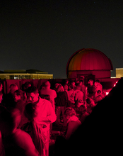 A large group of people on the roof of UIS Brookens Library at night with red lights.