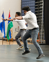 Two people in white shirts and jeans perform a synchronized dance on stage during a cultural event.