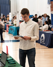 Young man reading a brochure at a busy indoor event with booths.