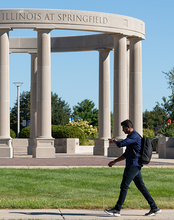 Person walking past a circular column structure with a clear blue sky.