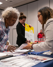 People interacting at a table with documents and supplies.