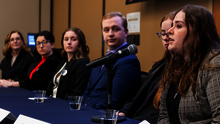 Panel of six people sitting at a table, one speaking into a microphone.