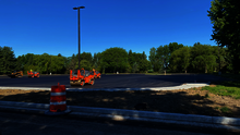 Paved parking lot under clear blue sky, surrounded by trees, with orange construction cones.
