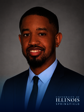 Smiling man in a suit and tie, University of Illinois Springfield logo.