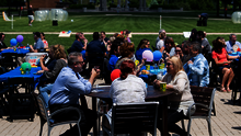 Outdoor gathering with people seated at tables, balloons, and sunny weather.