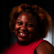 Smiling woman in a red top against a dark background.
