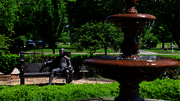 Fountain and bench with statues in a lush green park.