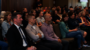 Audience attentively listening in a dimly lit conference room.