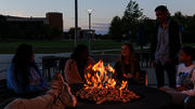 People gathered around a fire pit at dusk, smiling and talking.
