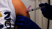 Vaccine injection into an arm by a person wearing blue gloves.