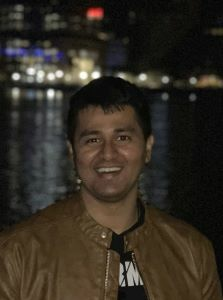 Sriram Krishnan standing in front of a river at night with tall city buildings behind him