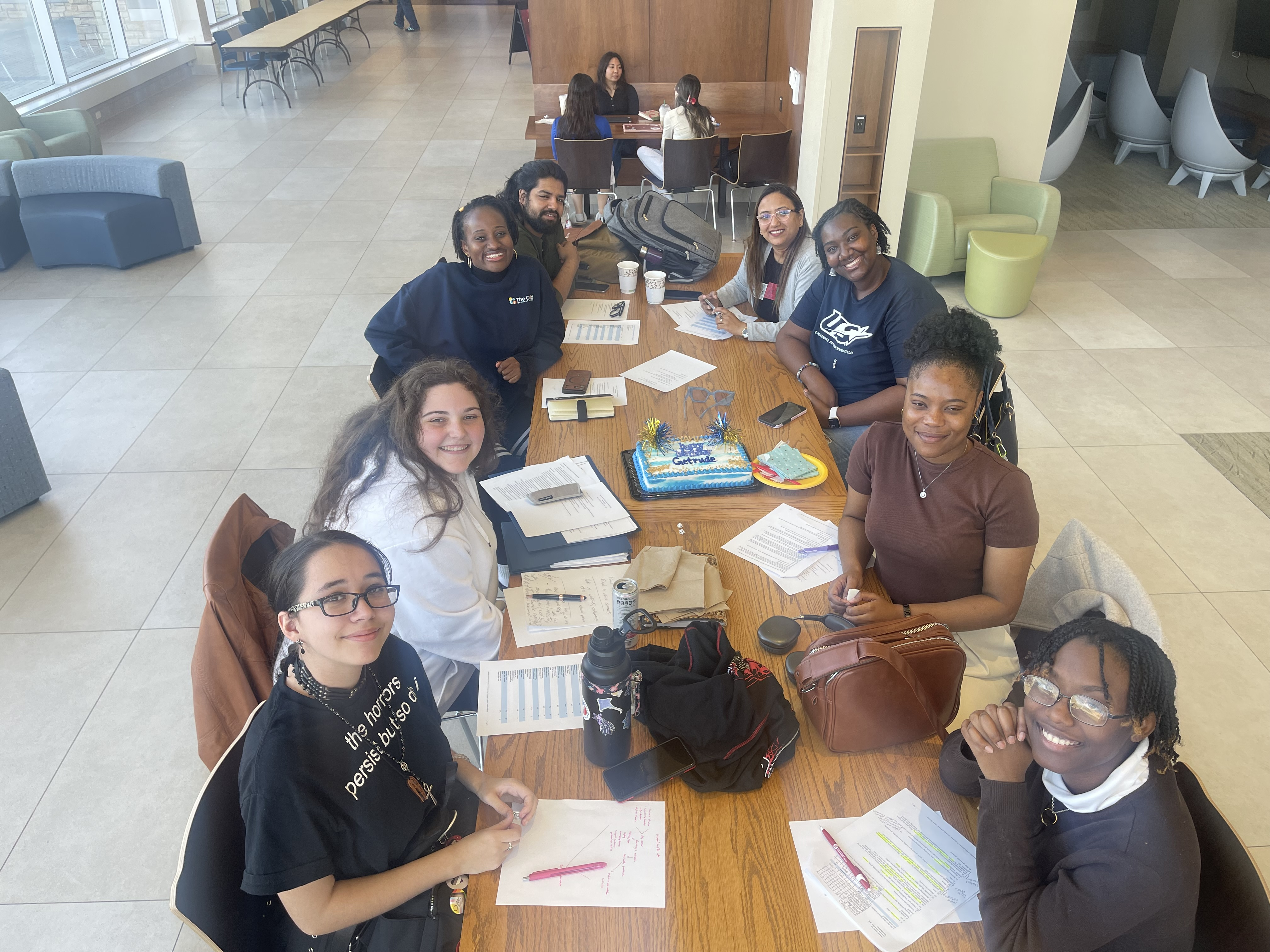 Group of students studying around a table, smiling, in a bright indoor setting.