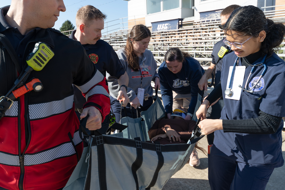 UIS and UIC students help Springfield fireman carry a person in a sling during a crisis response exercise on the UIS soccer field.